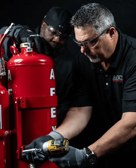 two men working on an AFEX fire suppression system with a black background